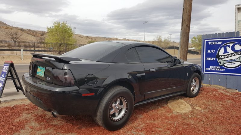 Black Mustang parked in front of the TC Automotive Repair sign with desert hills behind